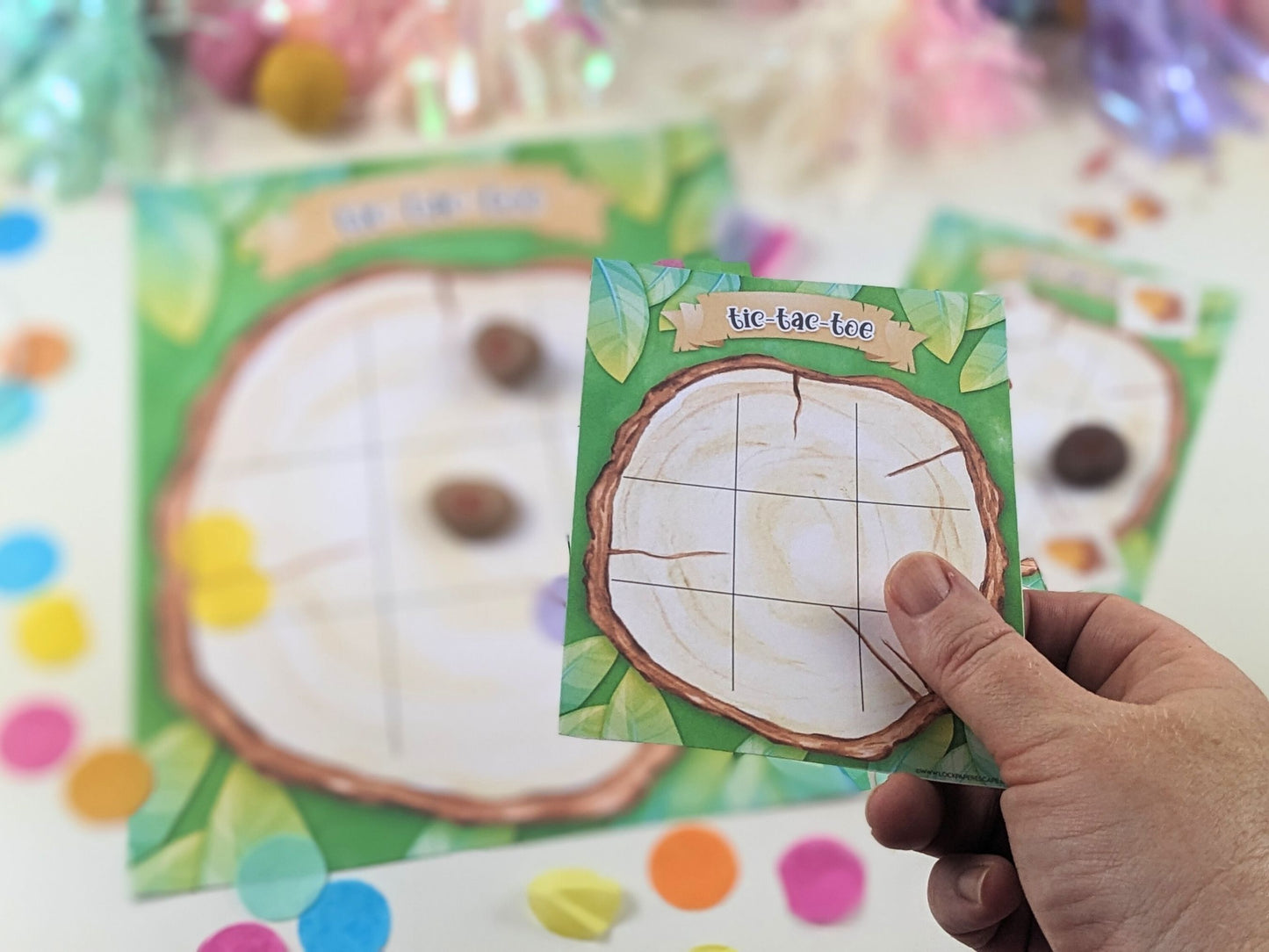 Hand holding a woodland tic-tac-toe game card with colorful background