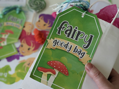 Green 'fairy goody bag' tag with mushroom design held by a hand, surrounded by colorful fairy-themed items.